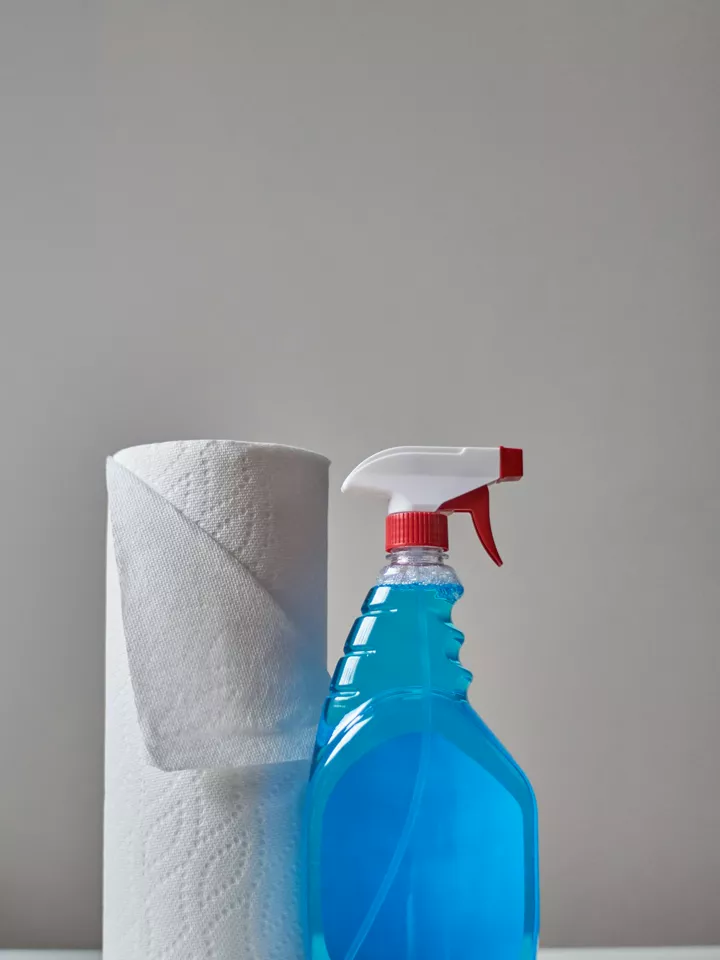 A spray bottle of blue cleaner next to a roll of paper towels