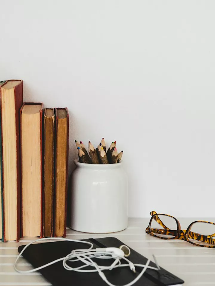 Books, a jar of pencils and reading glasses on a desk