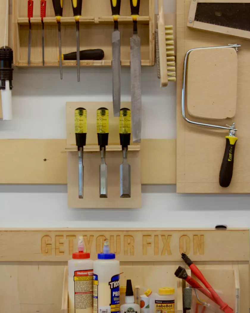 A workbench with chisels, saws and glue on a pegboard wall